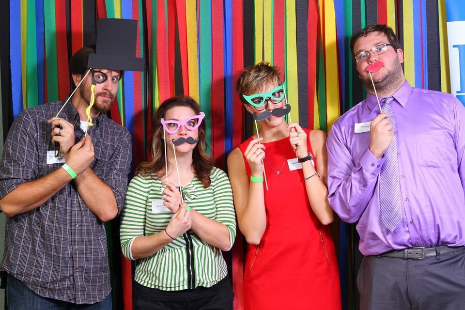 Four people holding fake glasses and fake mustaches to their face